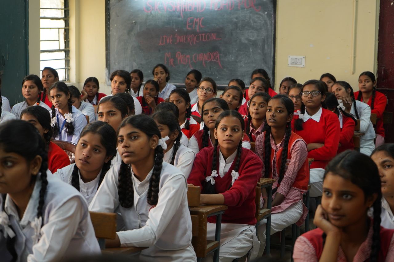 about-img Group of Indian schoolgirls in uniform attentively listening in a classroom setting.