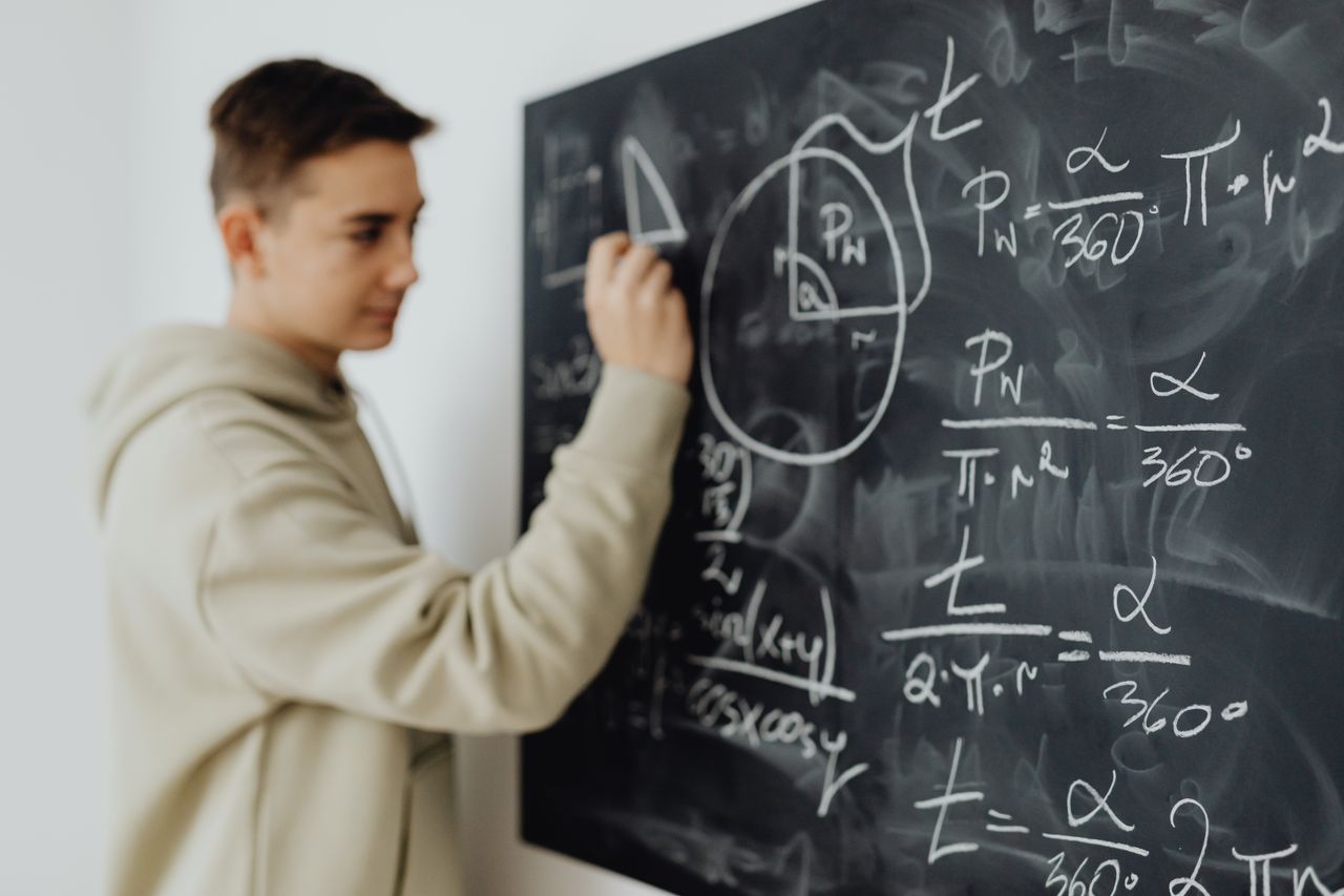 about-02 Focused teenager solving a math equation on a blackboard in a classroom setting.